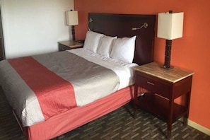 A hotel room with a bed, two bedside tables, a nightstand, and a lamp.