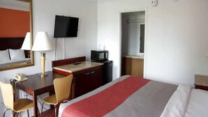Habitació d'hotel amb llit, escriptori amb cadira, televisió, microones i porta que dona a un bany.