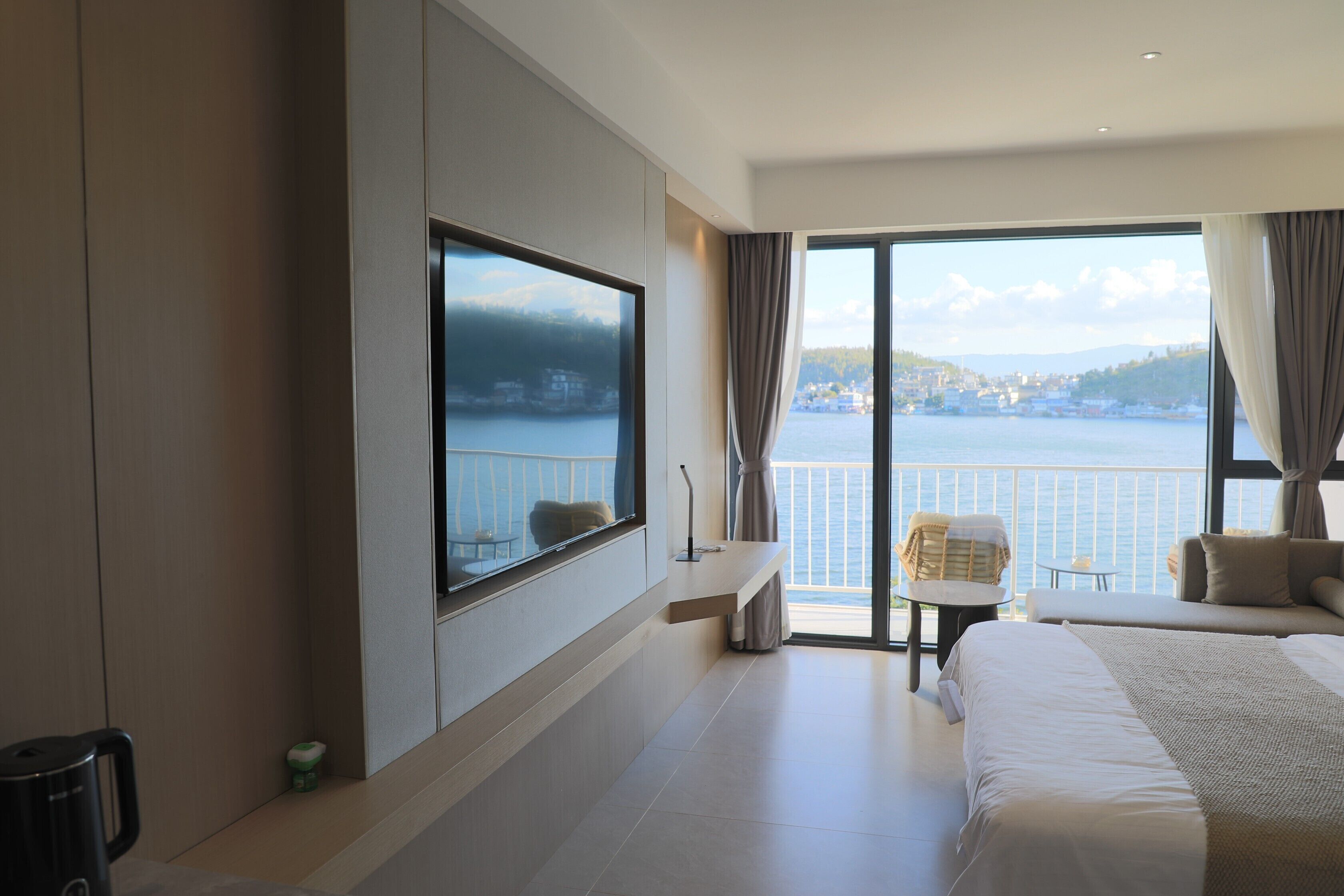 Una habitación de hotel con una cama grande, un televisor montado en la pared, un balcón con vistas al mar y una pequeña mesa.