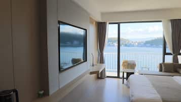 Una habitación de hotel con una cama grande, un televisor montado en la pared, un balcón con vistas al mar y una pequeña mesa.