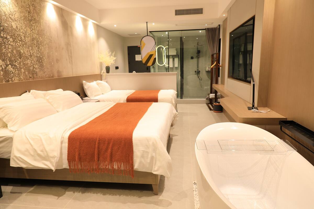 A modern hotel room with two beds, a large bathtub, and a glass shower area.