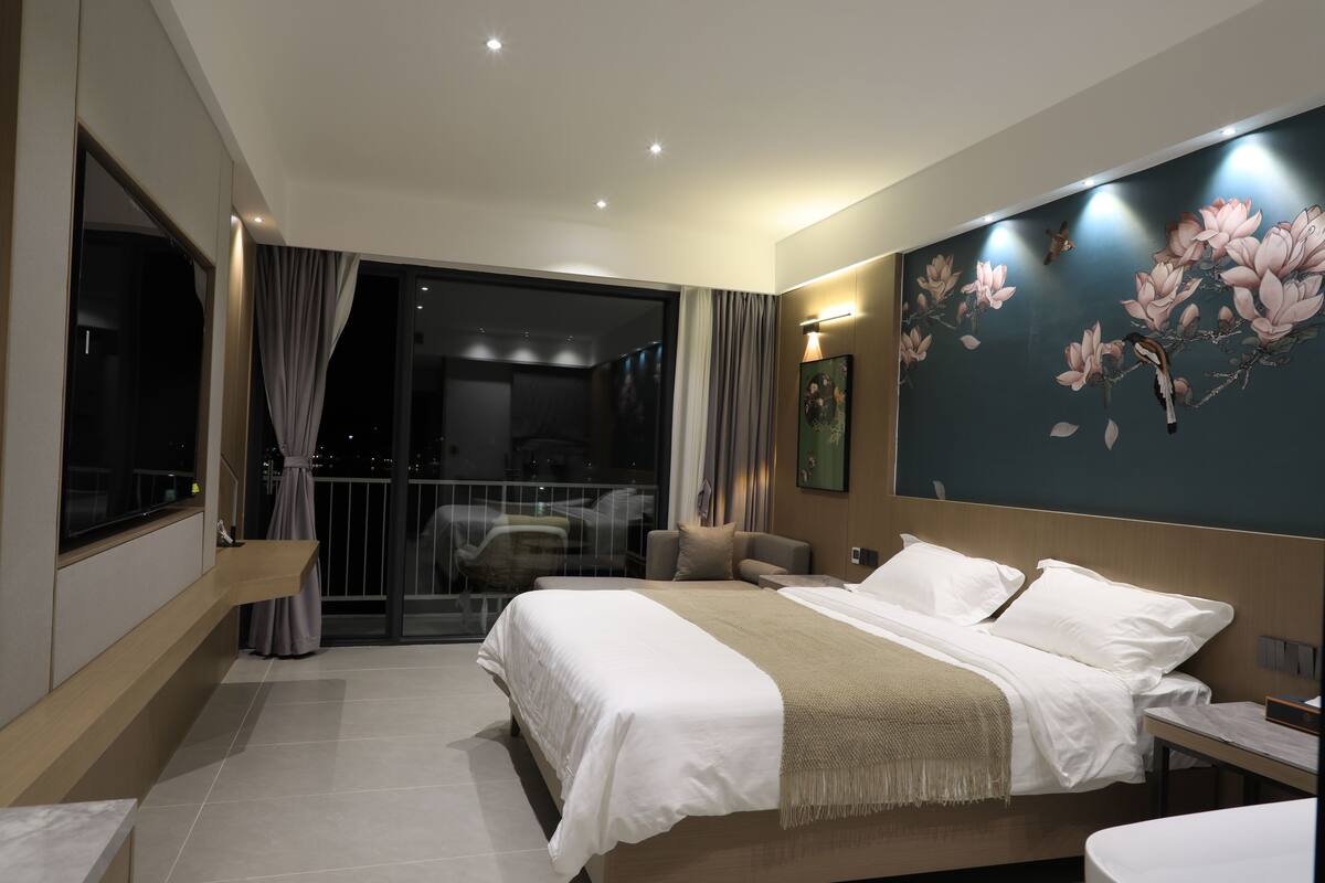 A modern hotel room with a large bed, a balcony with a view, and a decorative wall.