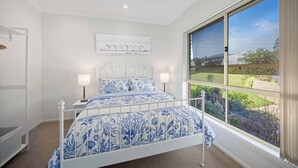 Un dormitorio con cama, lámparas de noche, ventilador de techo, ventana con vistas y una obra de arte colgada en la pared.