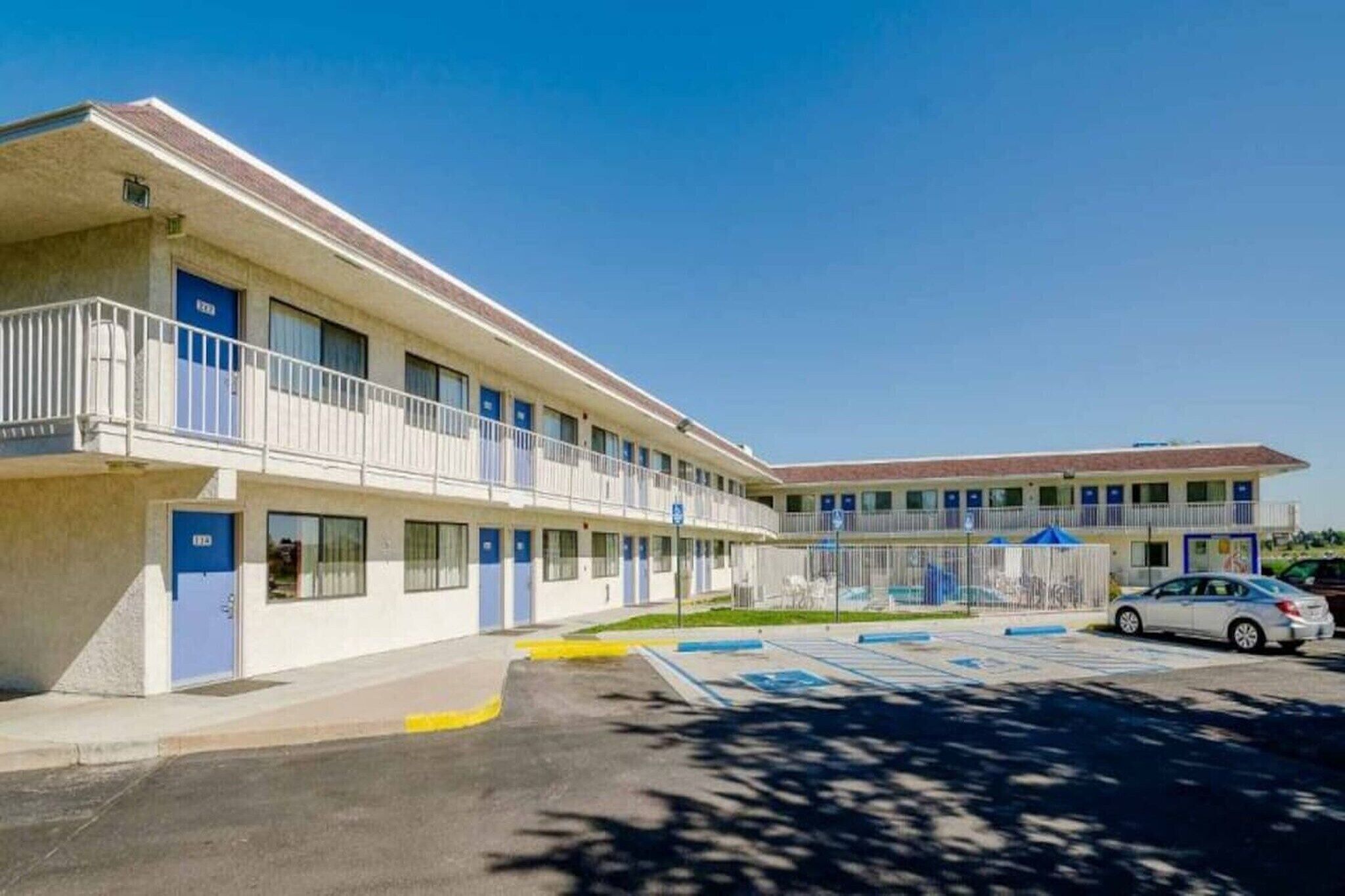 A motel with a two-story structure, a parking lot, and a clear blue sky.