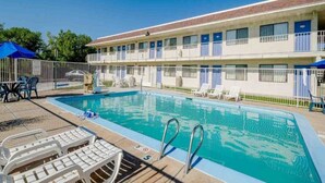 A motel with a swimming pool, outdoor chairs, and a fenced deck area. - 2 Full Beds | Non-Smoking (Thornton)
