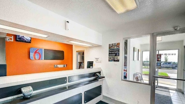 A reception area with a counter, a digital display, and a glass door leading outside. - 2 Full Beds | Non-Smoking (Thornton)
