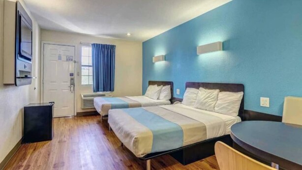 Habitación de hotel con dos camas, una mesita, televisor y ventana con cortinas.