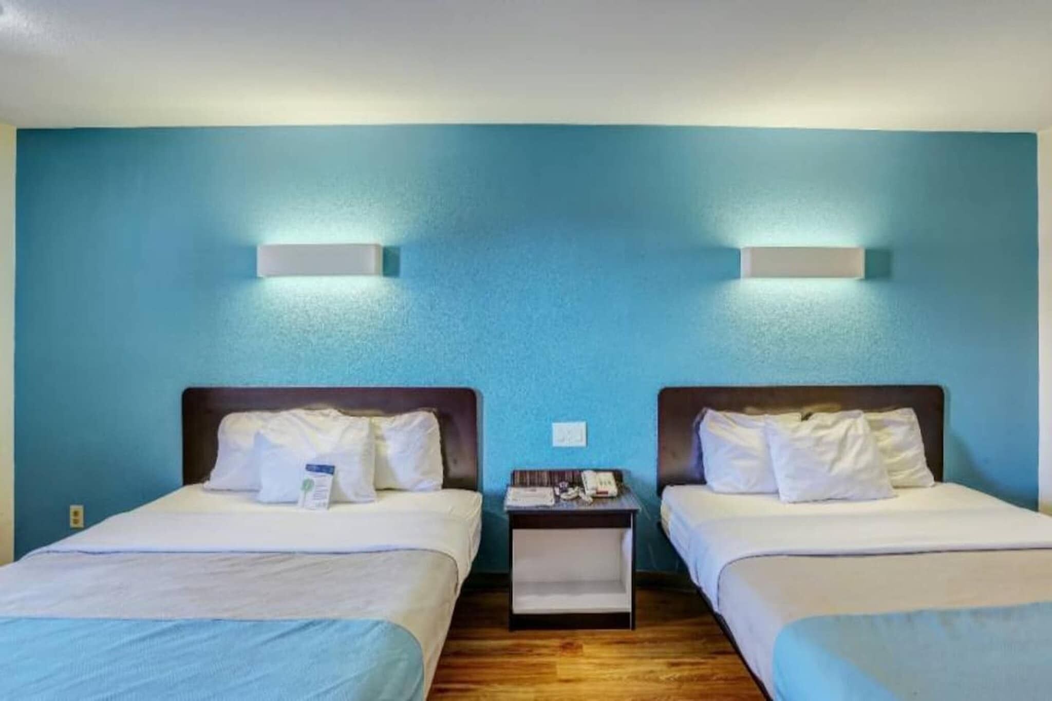 Two single beds with white bedding, a nightstand between them, and a blue wall.