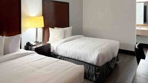 Une chambre d’hôtel avec deux lits, une table de chevet avec une lampe, un bureau et une chaise.