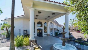 L’entrée d’un hôtel, avec un patio abrité, une fontaine et des sièges installés à l’extérieur.
