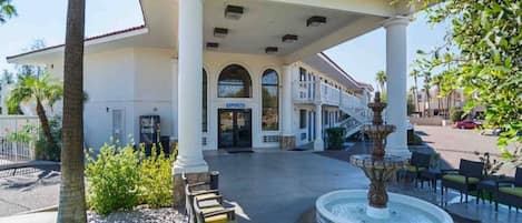 A hotel entrance with a covered patio, a fountain, and outdoor seating.