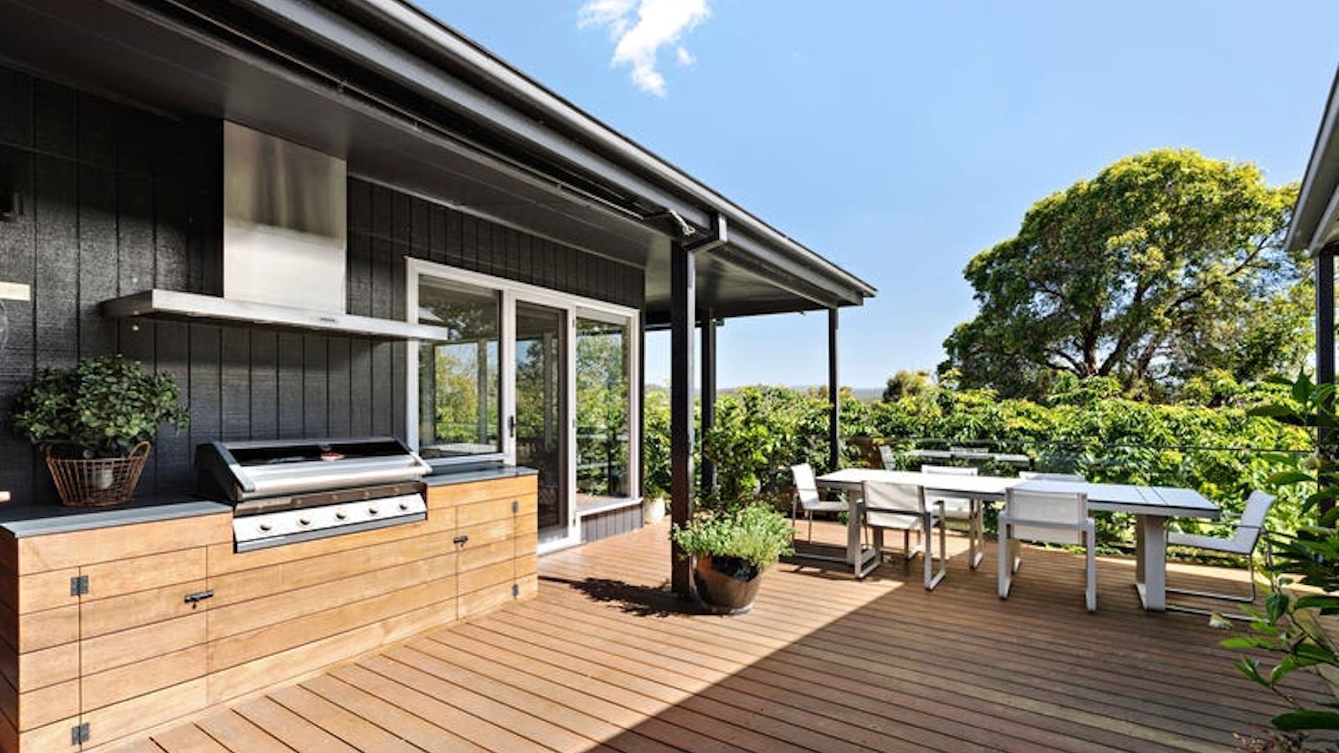 Une cuisine extérieure moderne, dotée d’un barbecue, d’une terrasse en bois et d’une table avec des chaises.