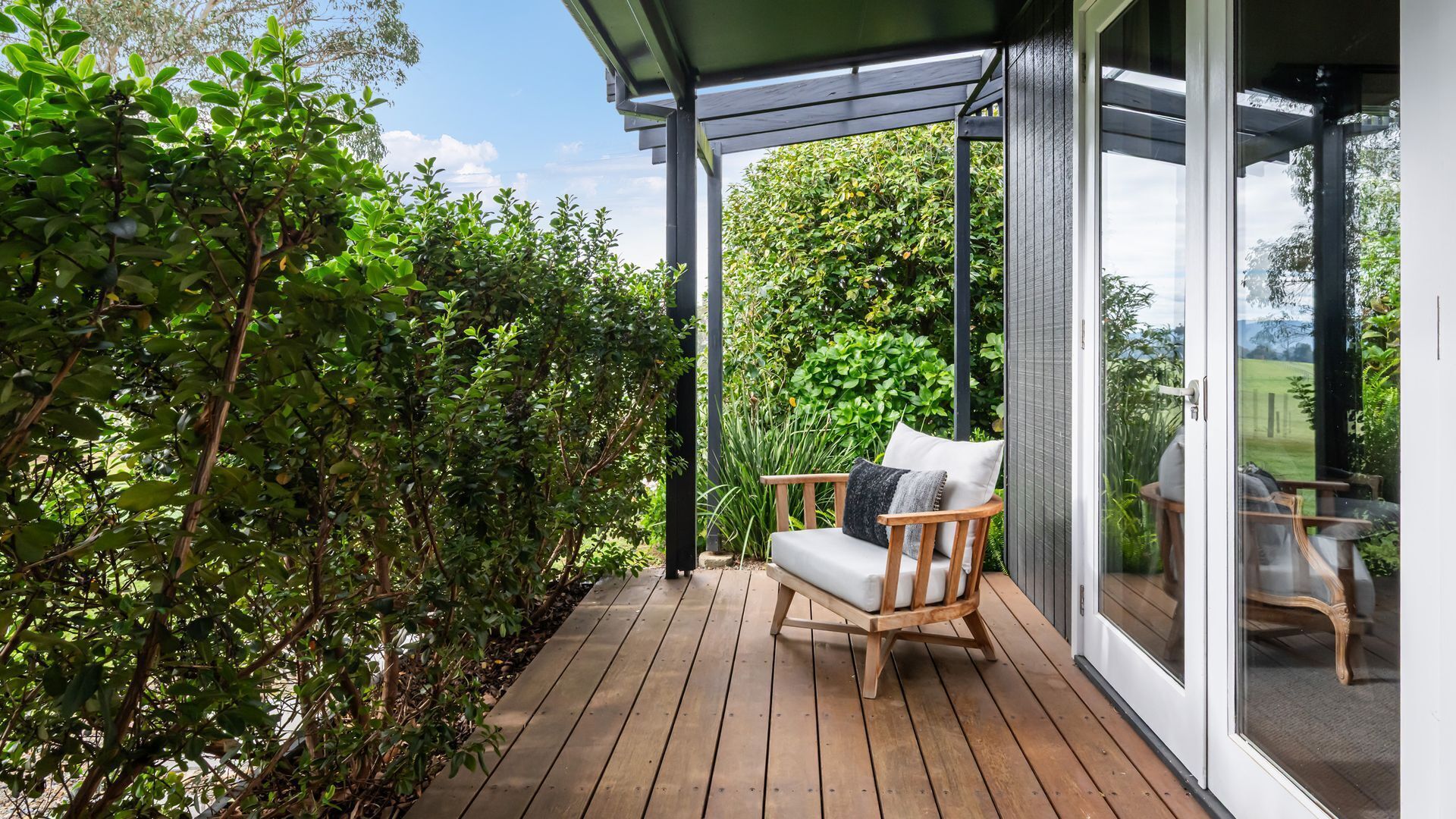 A wooden deck with a chair and a glass door leading to a garden.