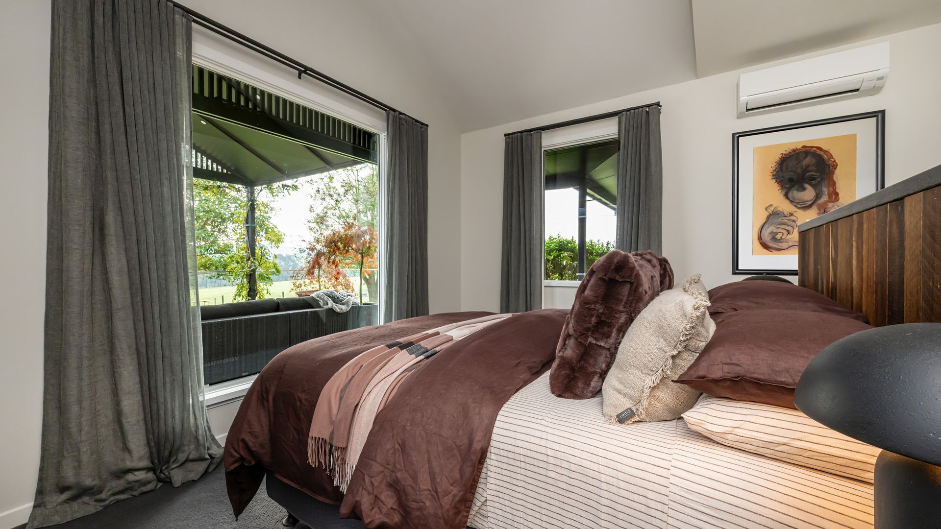 Une chambre à coucher avec un grand lit, une fenêtre avec des rideaux, un tableau au mur et un appareil de climatisation.