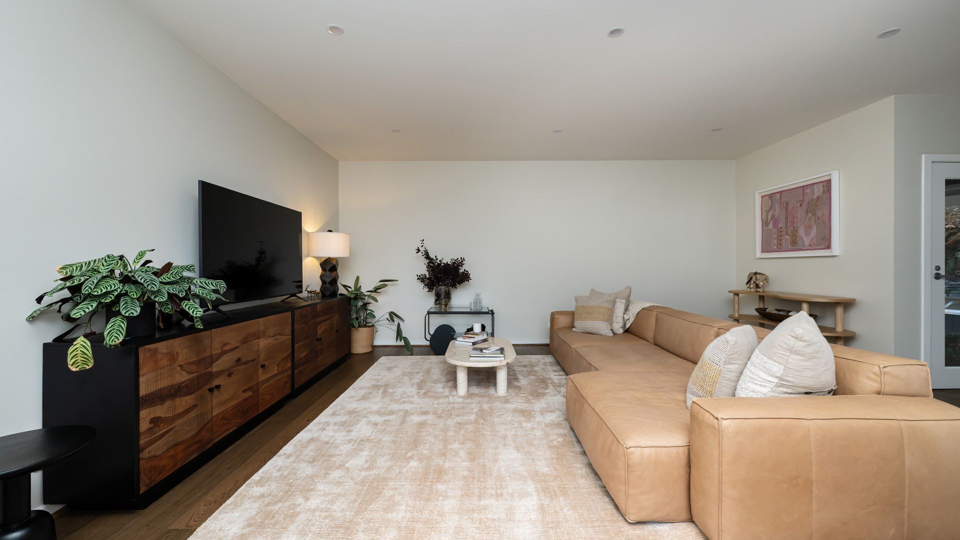 Ein modernes Wohnzimmer mit Flachbildfernseher, einer Couch, einem Couchtisch und Zimmerpflanzen.