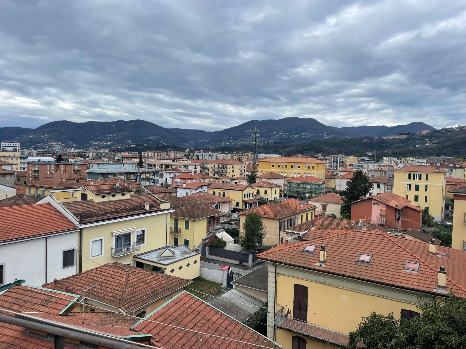 A cityscape with buildings, a mountain in the background, and a cloudy sky.