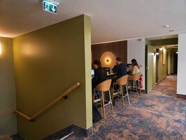 Un vestíbulo de hotel con una escalera, un área de descanso con mesas y un extintor.