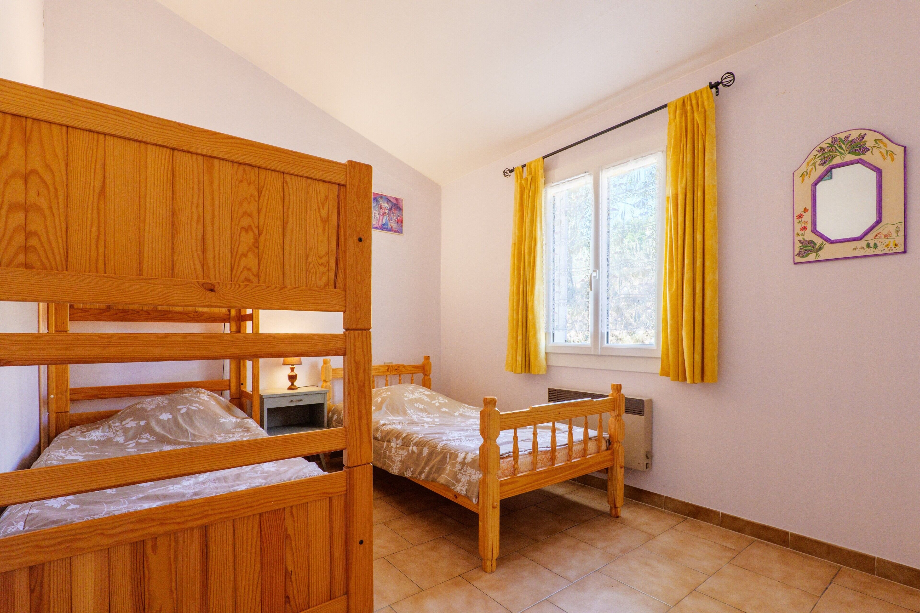 A room with bunk beds, a window with yellow curtains, a radiator, and a wall-mounted mirror.