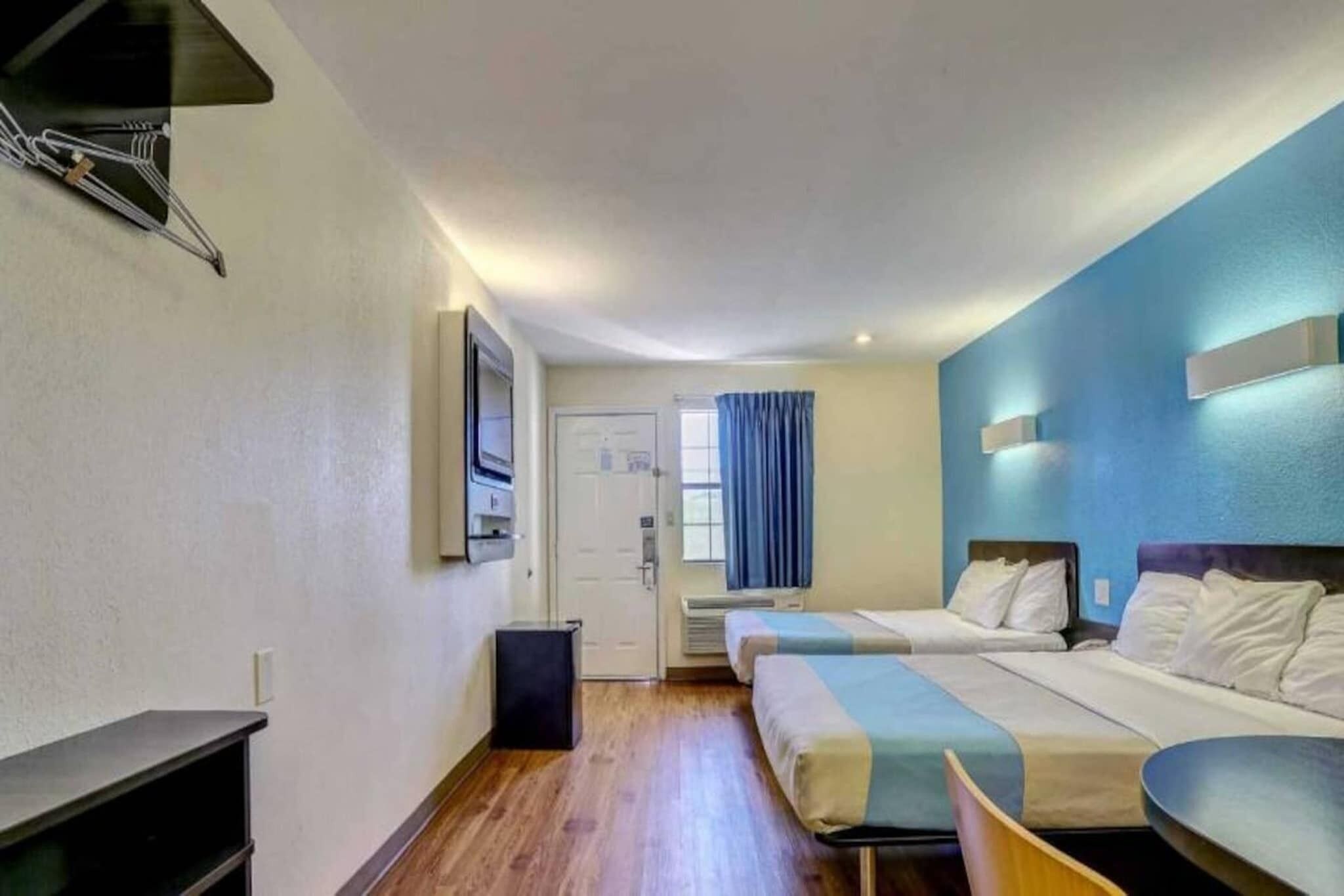 A hotel room with two beds, a desk, a chair, a TV, and a window with curtains.