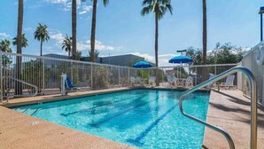 A swimming pool with a metal railing, palm trees, and outdoor seating.