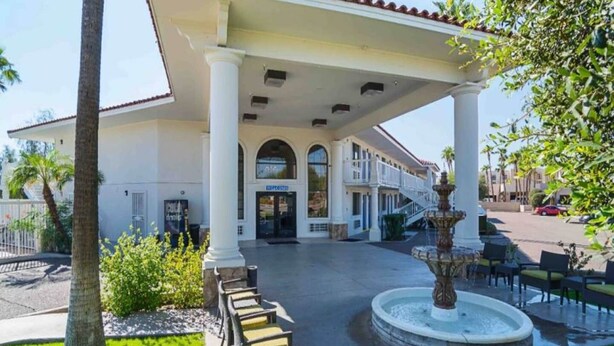 A hotel entrance with a covered patio, a fountain, and outdoor seating.