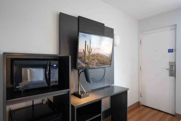 Una habitación con un televisor montado en la pared, un microondas sobre la encimera y una puerta con un cartel.