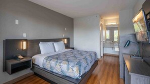 A modern hotel room with a large bed, bedside tables, a desk, and a mirror.