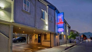 Un hotel con un llamativo letrero de neón, un acceso cubierto y una zona de estacionamiento.