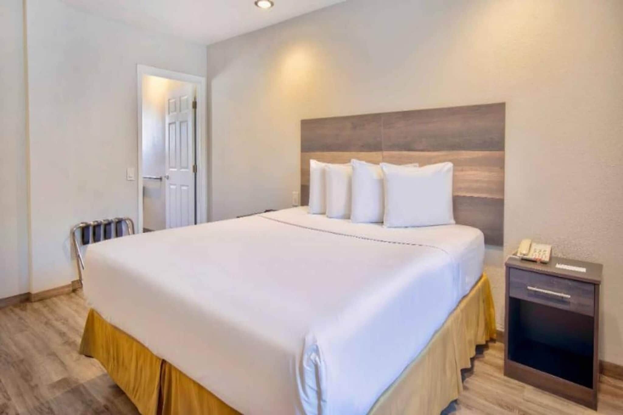 A hotel room with a large bed, a bedside table with a phone, and a door leading to another room.