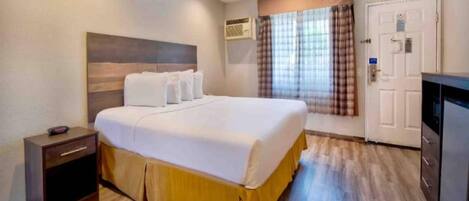 A hotel room with a bed, bedside table, wardrobe, and an air conditioning unit.