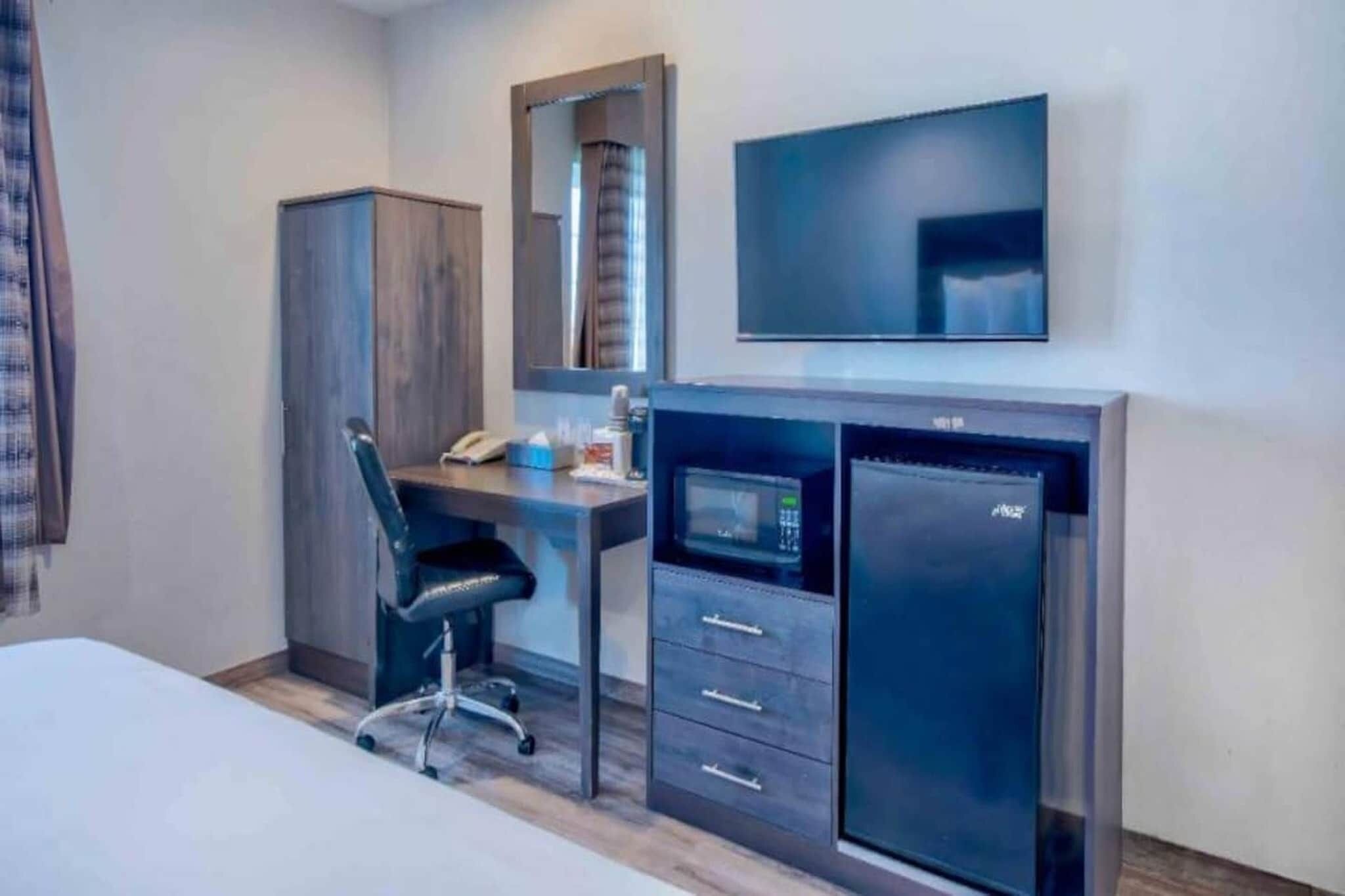 Une chambre d’hôtel comprenant un lit, un bureau avec une chaise, un minibar, une télévision et une armoire.