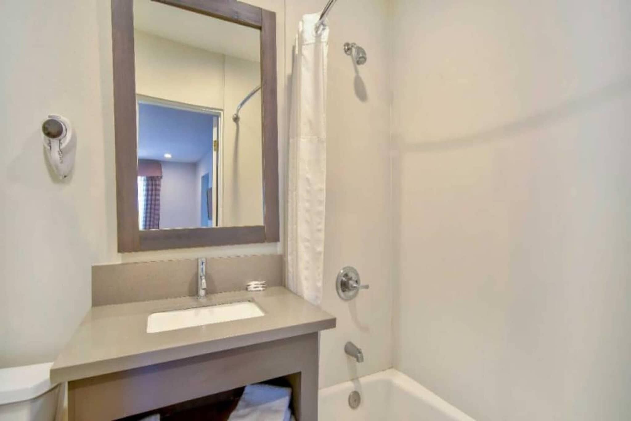 A bathroom with a sink, mirror, shower, and a visible door leading to another room.