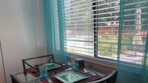 Une table à manger avec un plateau en verre, deux chaises et une fenêtre avec des stores.