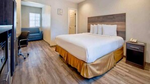 A hotel room with a bed, a desk, a chair, a wardrobe, and a bedside table with a phone.