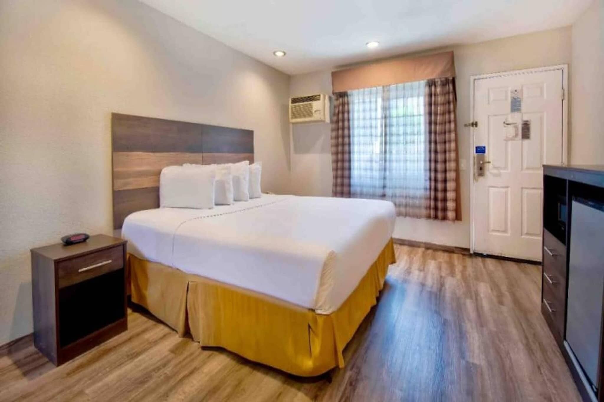 Una habitación de hotel con cama, mesita de noche, armario y unidad de aire acondicionado.