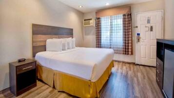 Una habitación de hotel con cama, mesita de noche, armario y unidad de aire acondicionado.