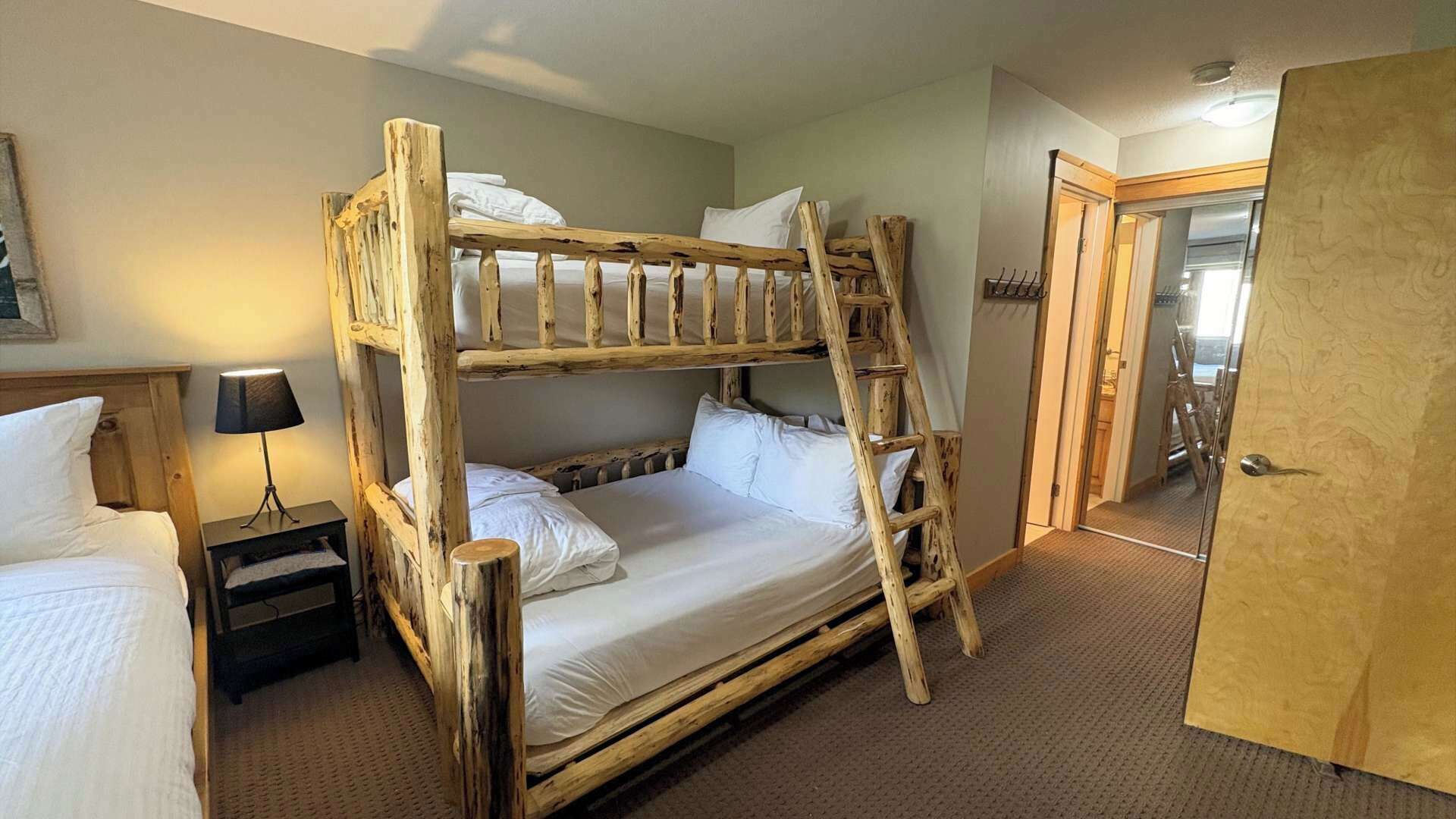 A bunk bed with a ladder, a bedside table with a lamp, and a door to another room.