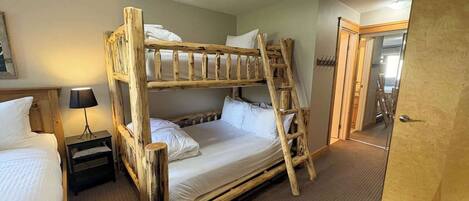 A bunk bed with a ladder, a bedside table with a lamp, and a door to another room.