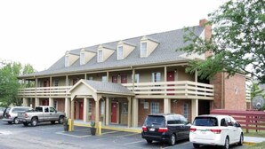 A multi-story hotel with a central entrance, a parking lot with several cars, and a brick facade. - 1 Queen Bed | Non-Smoking (Dayton)