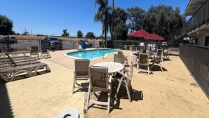 Ein Poolbereich mit Liegestühlen und Tischen, einem roten Sonnenschirm und einer umzäunten Terrasse.