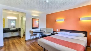 Ein Hotelzimmer mit Bett, Nachttisch, Sessel und kleinem Schreibtisch mit Stuhl.