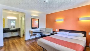 Ein Hotelzimmer mit einem Bett, einem Schreibtisch mit Stuhl, einem Badezimmer und einem Spiegel.
