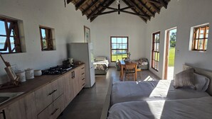 A room with a bed, a small table, a chair, a kitchen area with a stove, and a refrigerator.