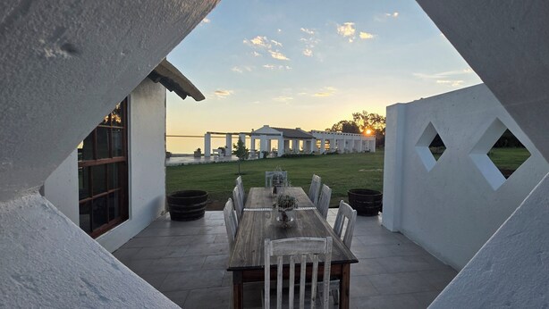 A dining area with a table and chairs, a view of a building with columns, and a grassy area.