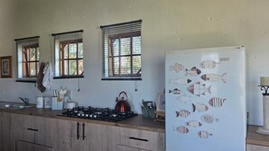 A kitchen with wooden cabinets, a gas stove, a refrigerator with fish decals, and three windows with blinds.
