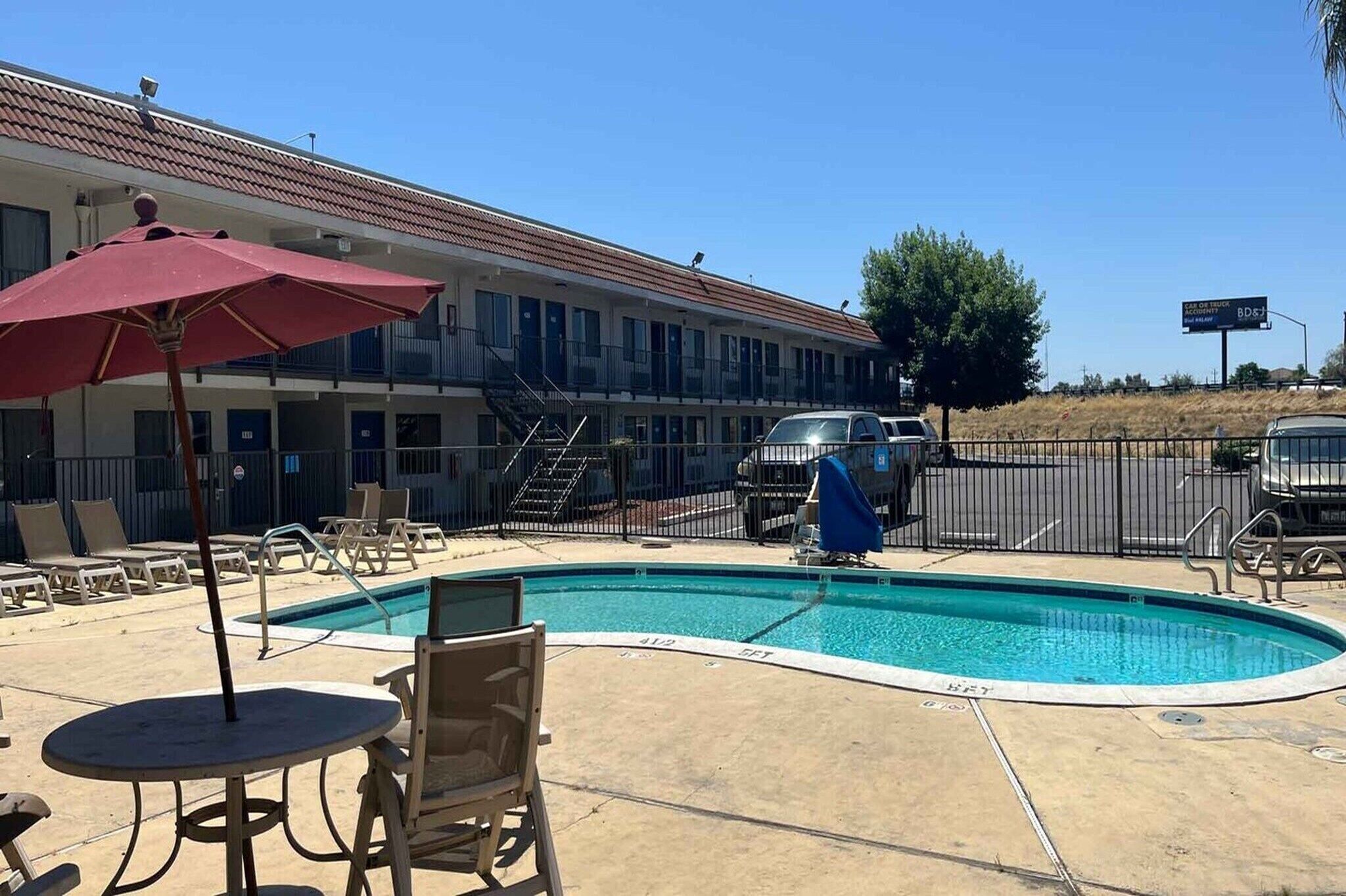 A motel with a swimming pool, outdoor seating, and a covered area with an umbrella.