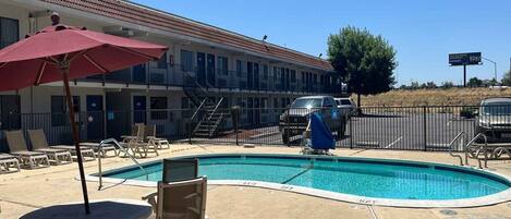 A motel with a swimming pool, outdoor seating, and a covered area with an umbrella.