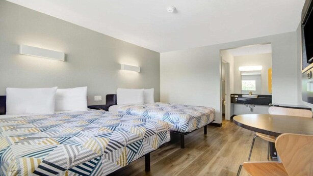 Hotellihuone, jossa on kaksi sänkyä, pieni keittonurkkaus, ruokapöytä ja peili.