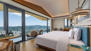 A modern hotel room with a large bed, a dining area, and a balcony with a city view.