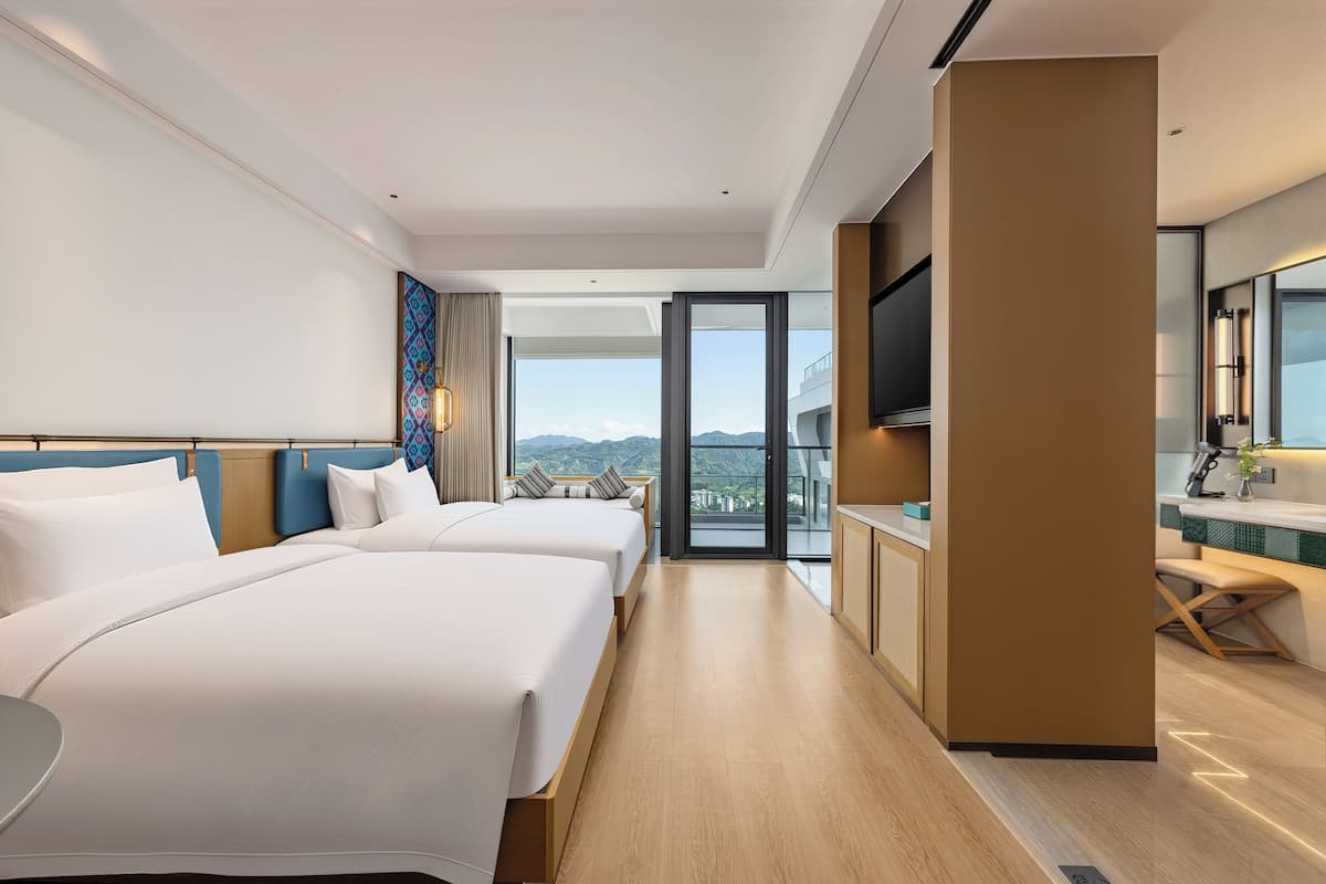 A hotel room with two beds, a TV, a balcony with a view, and a kitchenette.
